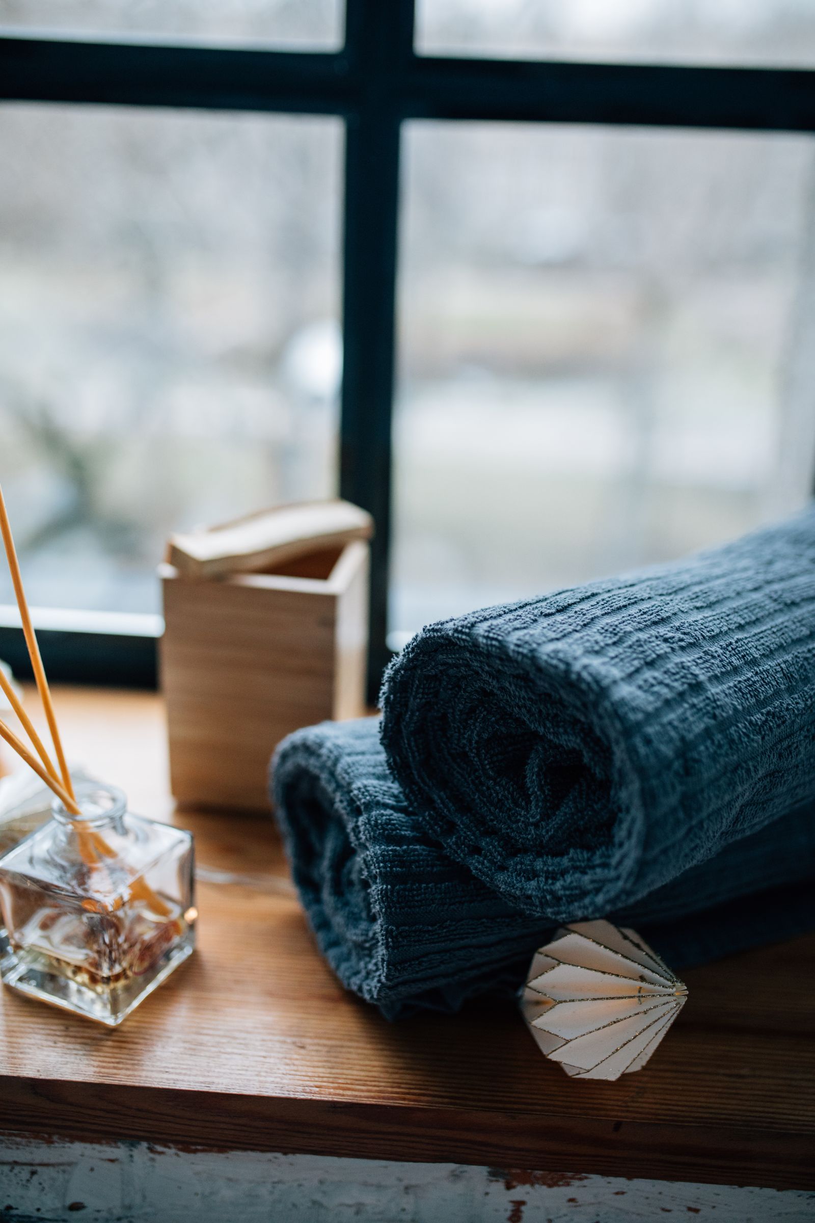 Rolled towels and a reed diffuser in soft window light